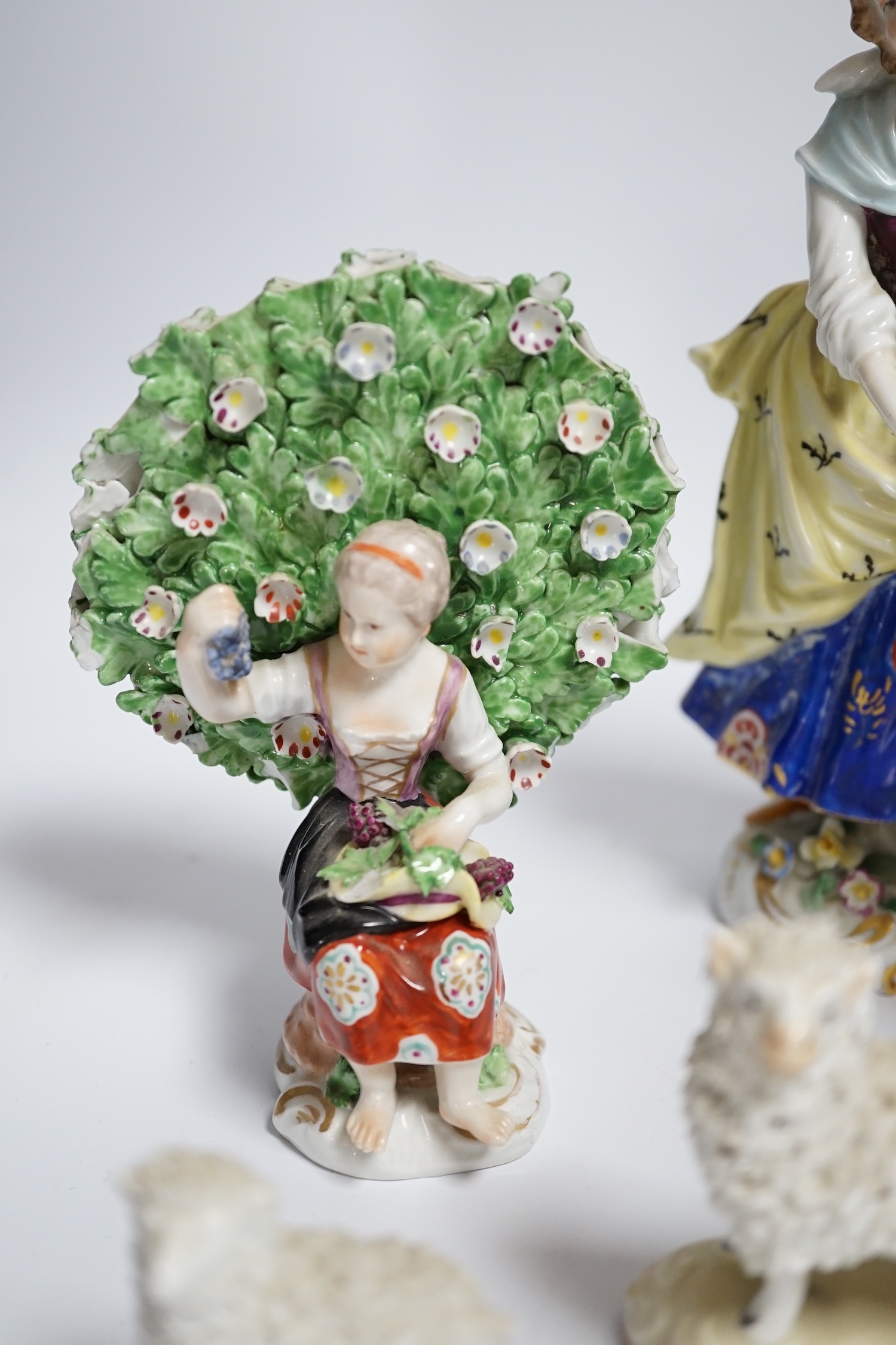 A pair of Derby style porcelain small bocage figures, a boy and girl seated with grape filled hats, height 14cm, three porcelain lambs and another figure